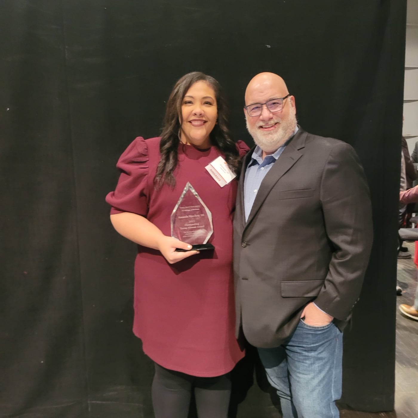 Amanda Matchett holding a glass achievement award, standing beside a presenter